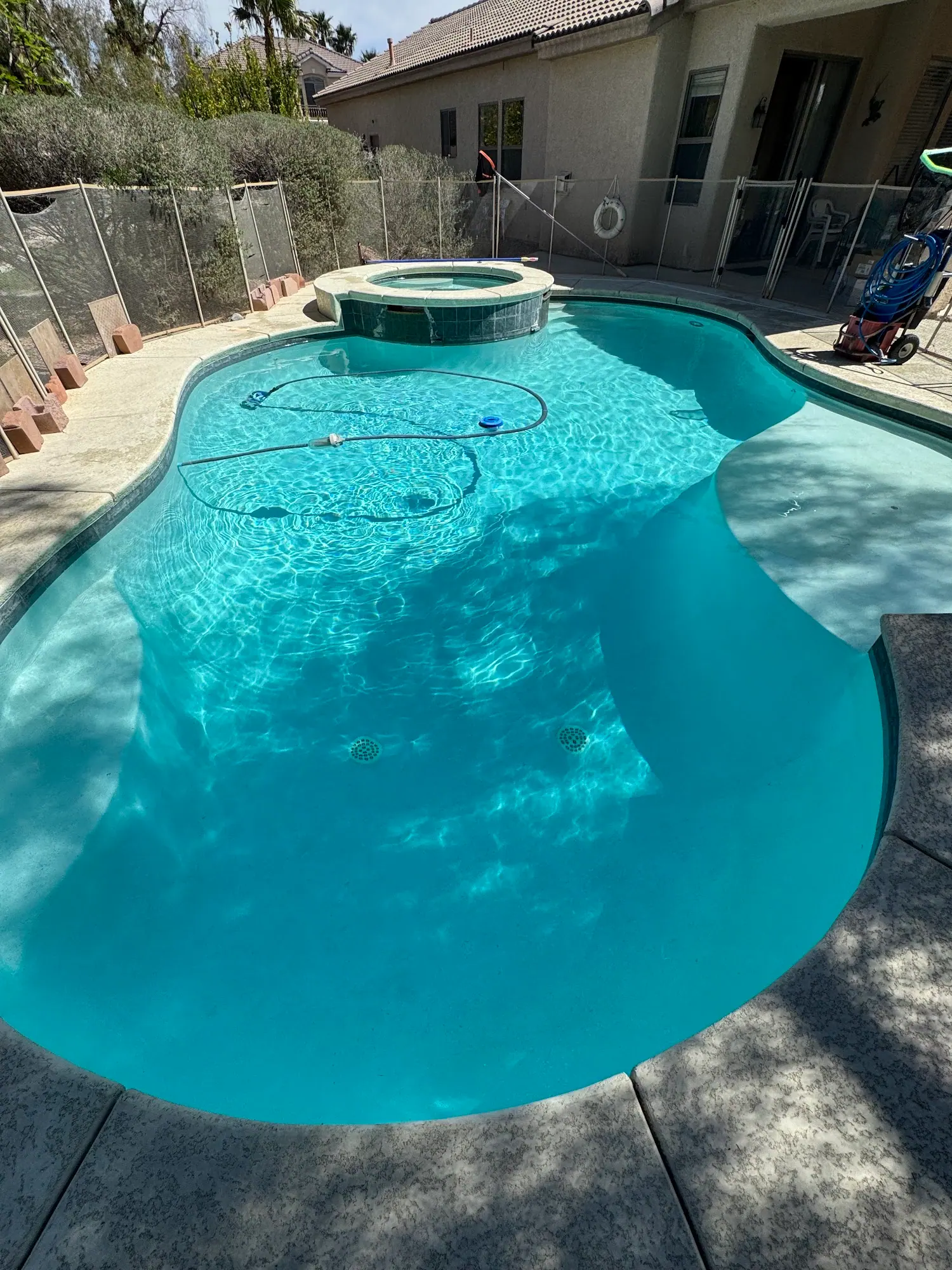 A clear turquoise pool with a robotic cleaner on the floor, a spa at the far end and a walled backyard